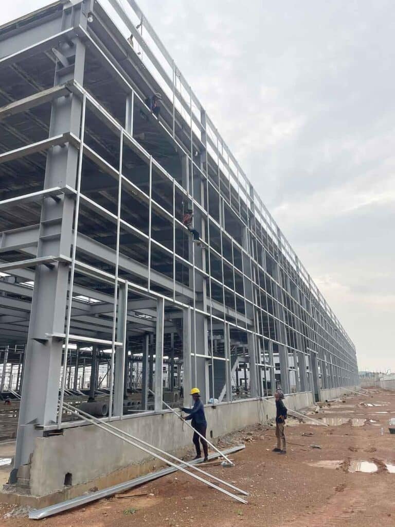 Construction workers installing exterior horizontal wall girts on a multi-story Metal Building, showcasing the precise assembly of a prefabricated metal building