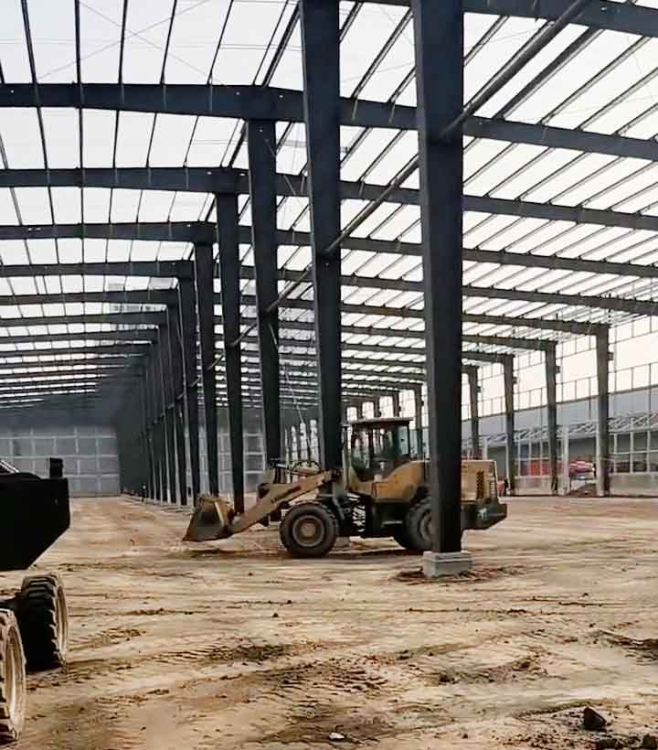 Perspectiva profunda de las columnas negras alineadas que conforman la estructura modular de una nave industrial prefabricada de acero con un tractor en el centro.