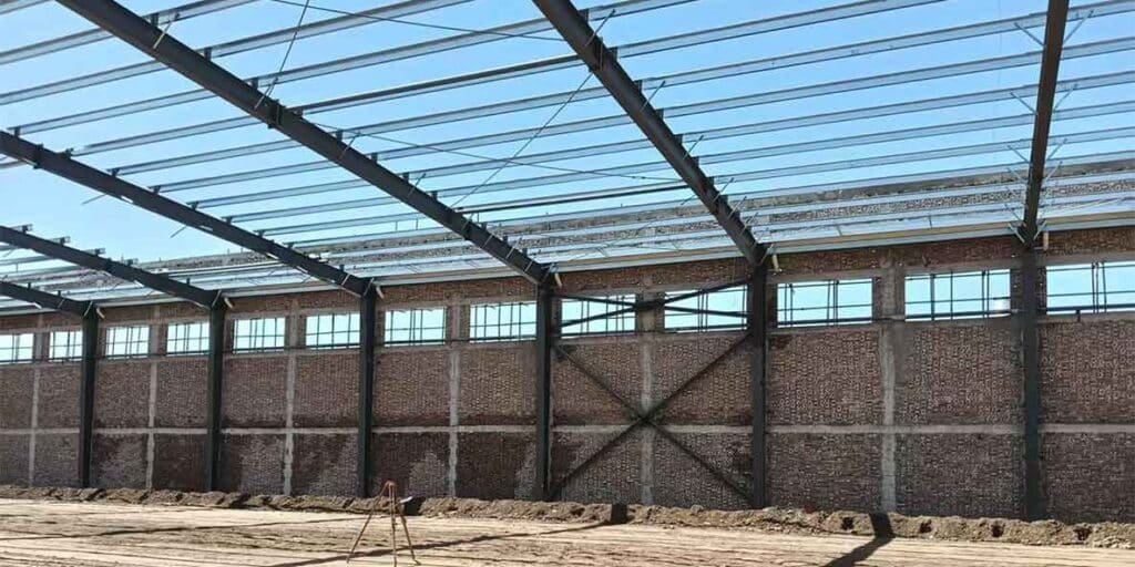 Un trípode de topógrafo descansa sobre el amplio suelo de tierra, preparándolo para el vertido de concreto en el interior de lo que serán bodegas modernas.
