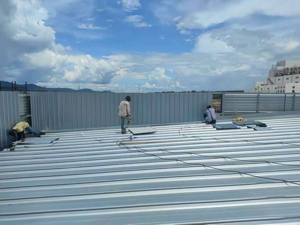 Workers installing corrugated steel roof panels on top of a vast Metal Building, ensuring heavy-duty weatherproofing for an industrial metal building.