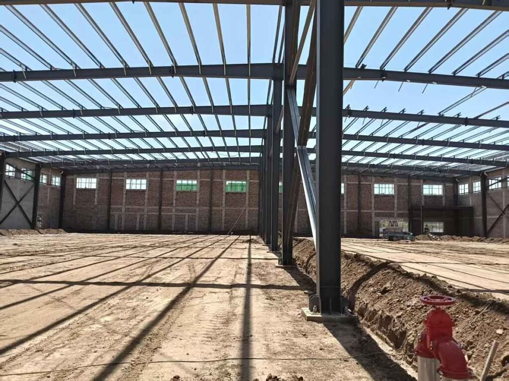 Interior en fase de tierra mostrando soluciones industriales, incluyendo una gruesa válvula roja de agua en primer plano y una línea de dobles columnas de acero.