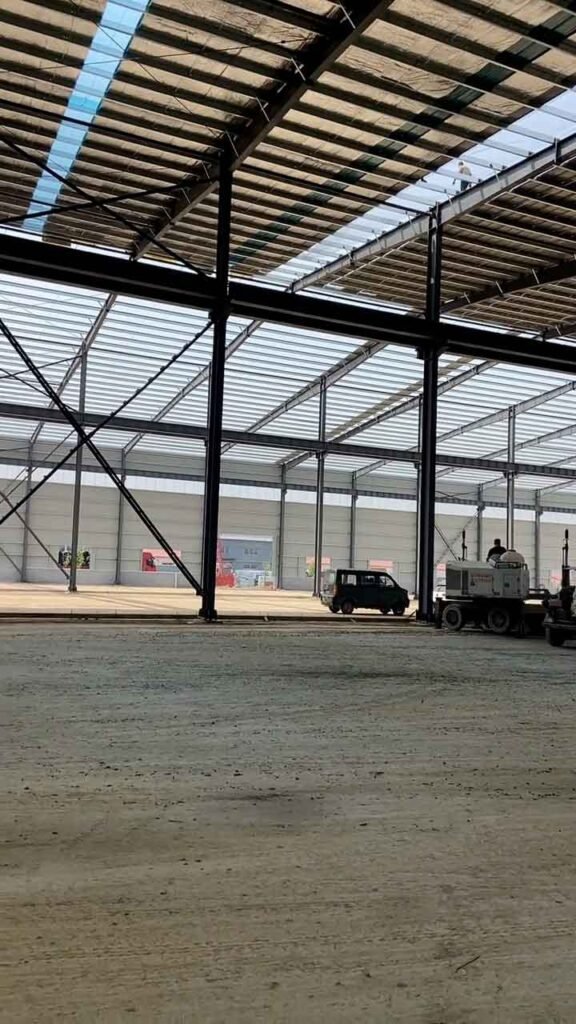 Cerramientos y esqueleto de una bodega metálica industrial en etapa de acabados laterales y cimentación.