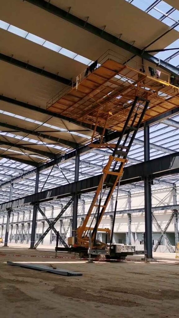 Trabajadores operando una gran plataforma elevadora de tijera amarilla instalando paneles de techo, demostrando una construcción industrial eficiente.