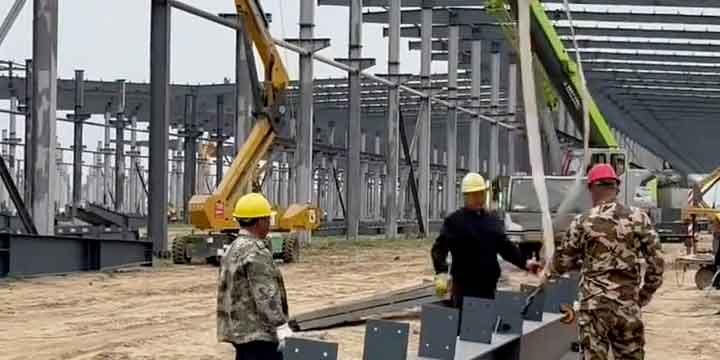 Operarios utilizando plataformas elevadoras de tijera para instalar rápidamente paneles sándwich prefabricados en la fachada de una nave, ilustrando el método de construcción industrial rápida.