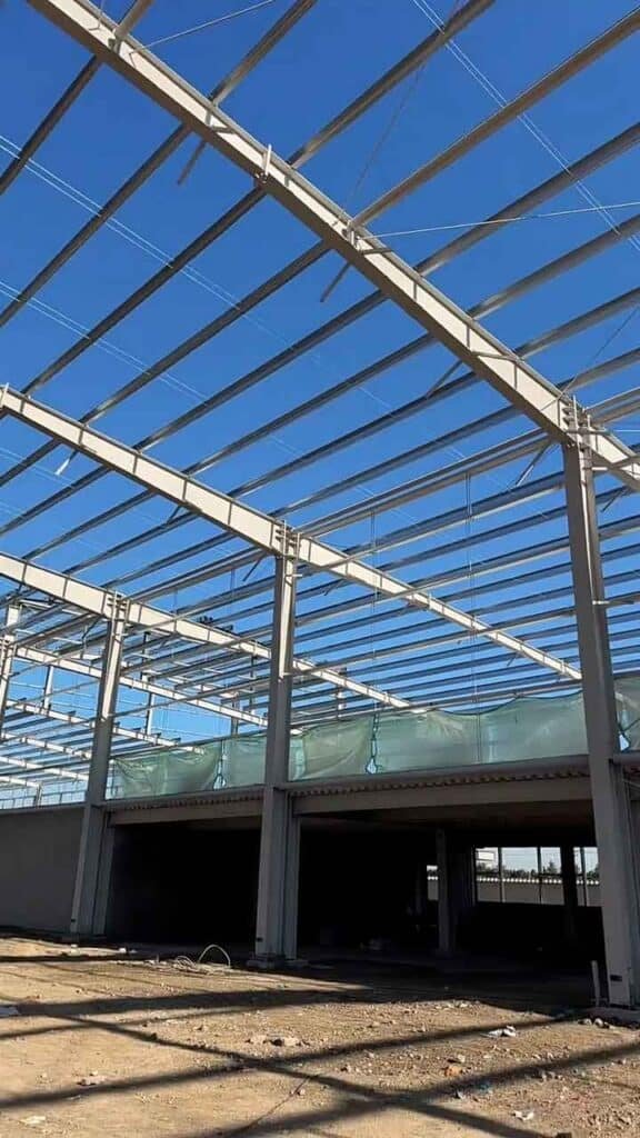 Fase avanzada de construcción industrial rápida con columnas blancas y áreas de entrepiso definidas.