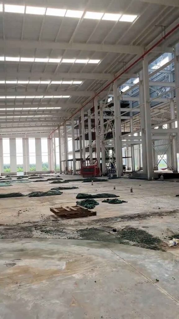 Proceso de construcción industrial rápida evidenciado por el montaje de una estructura secundaria de múltiples niveles (mezzanine) en el interior, utilizando un elevador de tijera rojo.