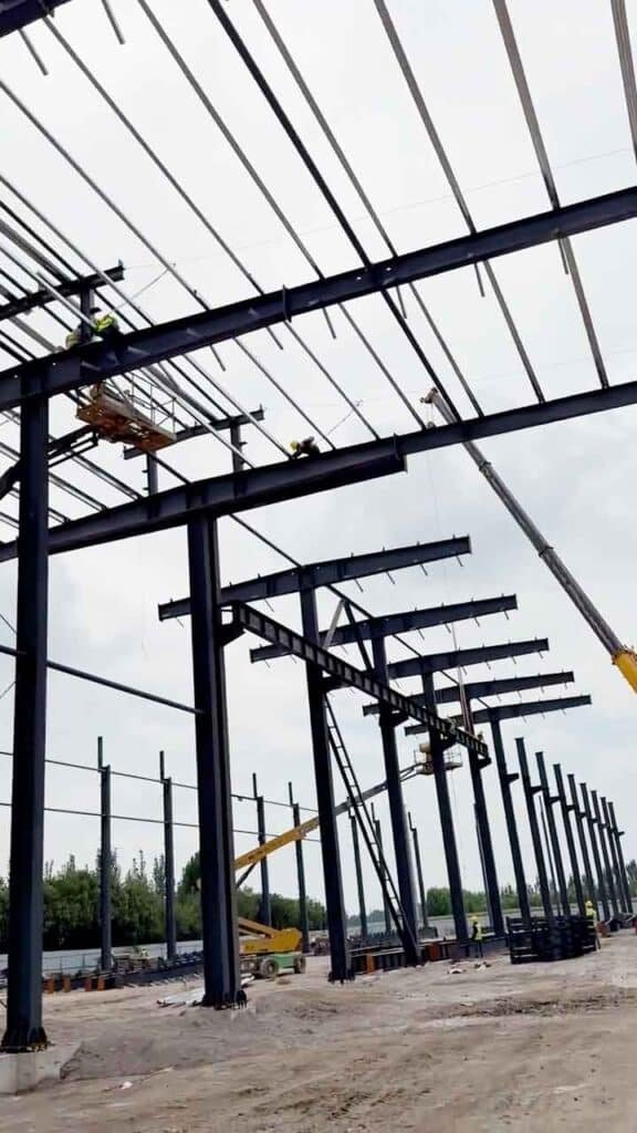 Trabajadores realizando montaje de techumbre en un proyecto de construcción industrial rápida con plataformas de elevación.