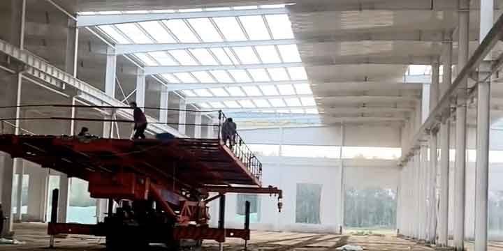 Plataforma elevadora roja trabajando en la terminación de la techumbre de un custom steel building supplier para un proyecto a medida.