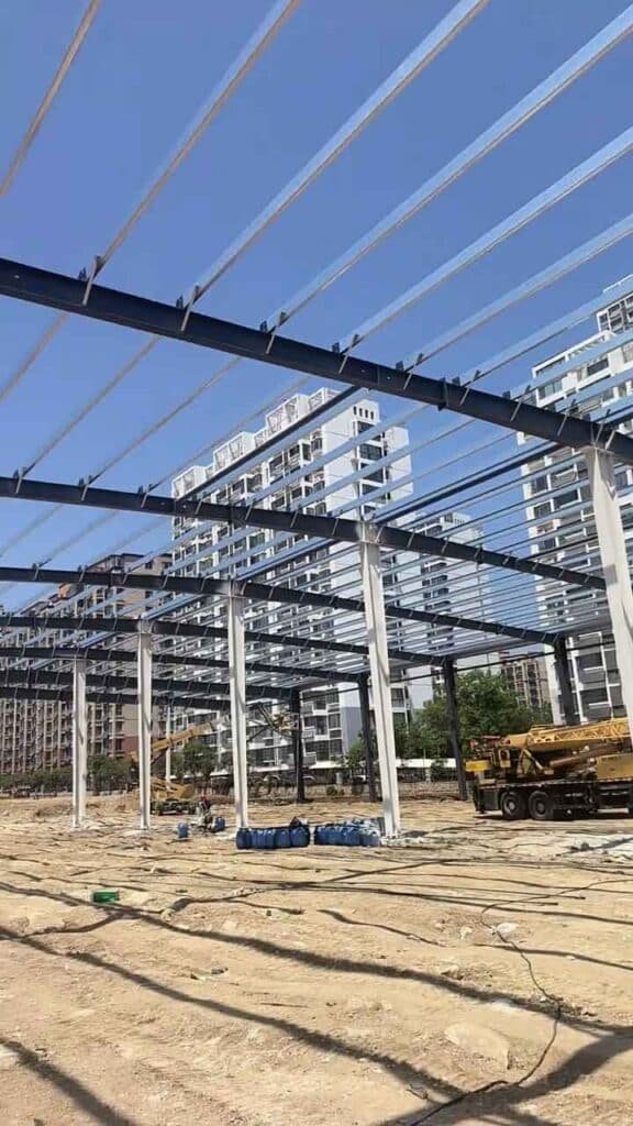 Obra de construcción de un depósito industrial de acero con grúas de gran tonelaje operando en el sitio.
