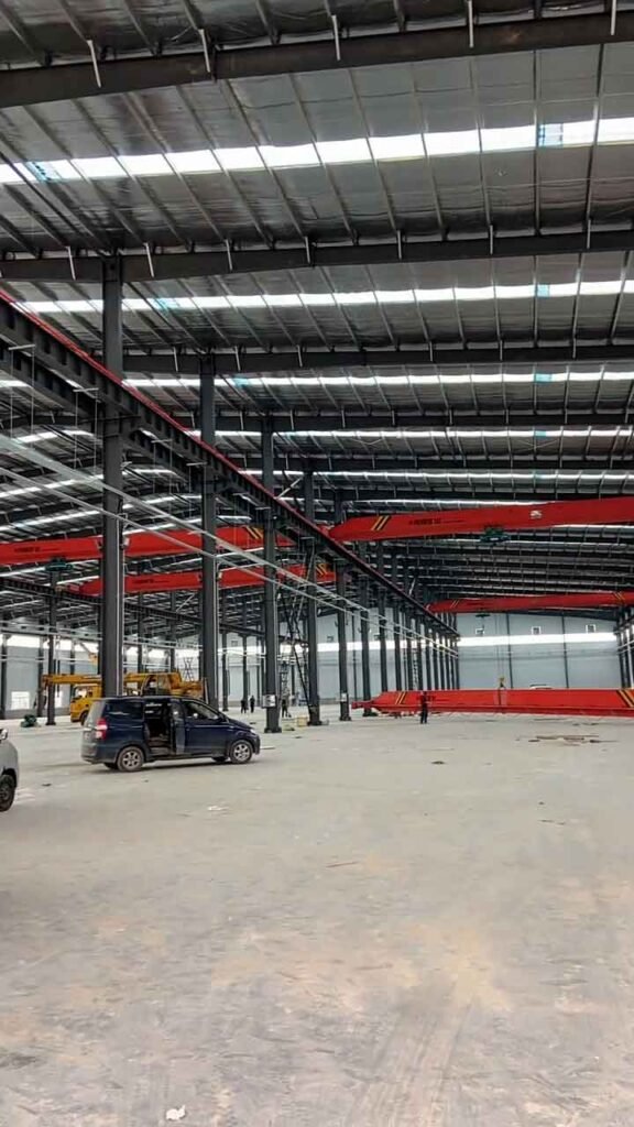Estructura de edificio de acero industrial con sistemas de carril para grúas viajeras y acceso vehicular.