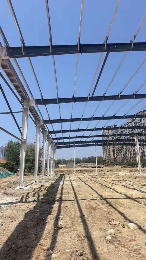 Perspectiva de columnas blancas alineadas de una estructura metálica industrial sobre terreno preparado para pavimentación.