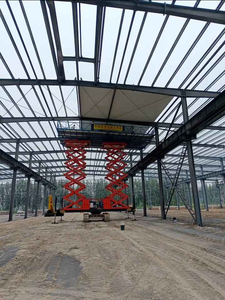 Elevación de una estructura metálica industrial utilizando una plataforma de tijera roja para el montaje de vigas y correas de techumbre.