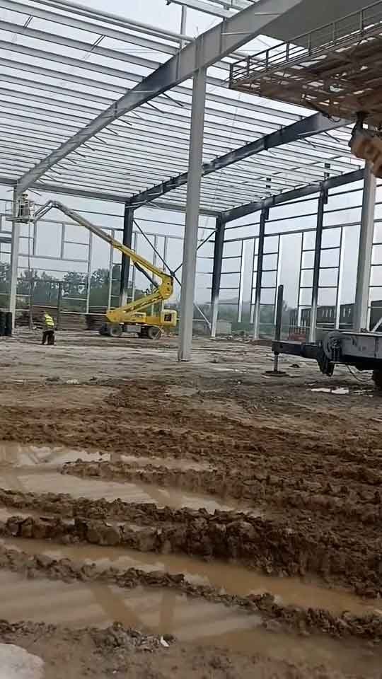Maquinaria de elevación tipo manlift amarilla trabajando en la instalación de una estructura metálica industrial de gran altura.