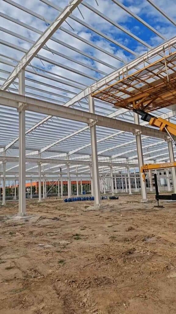Perspectiva de pórticos de acero blanco alineados en una obra dirigida por un fabricante de edificios industriales metálicos profesional.