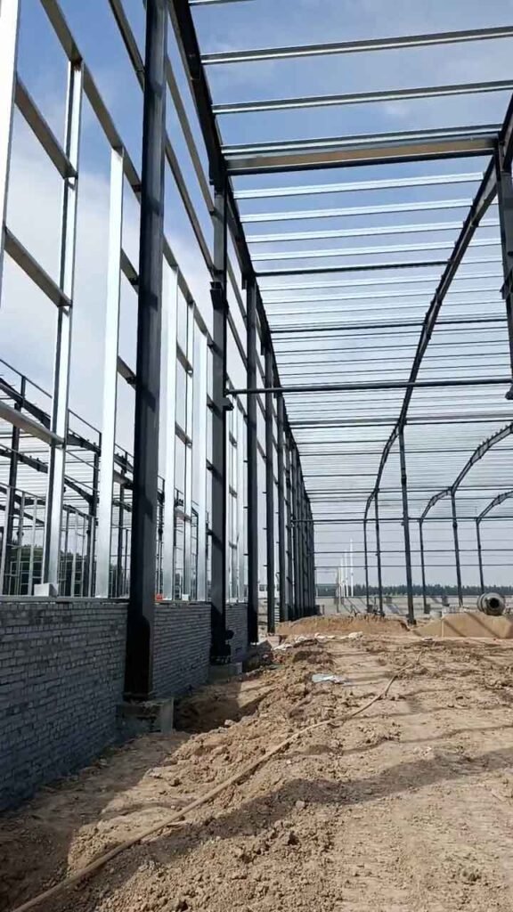 Muro perimetral de ladrillo y columnas de acero de un galpón industrial metálico en etapa de cerramiento.