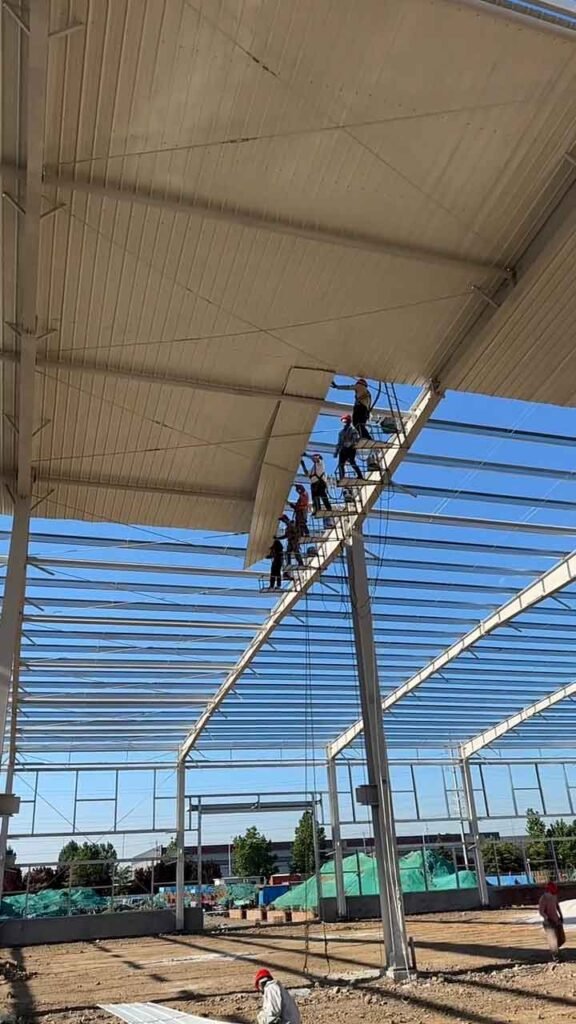 Trabajadores instalando paneles de cubierta en un galpón industrial prefabricado de acero