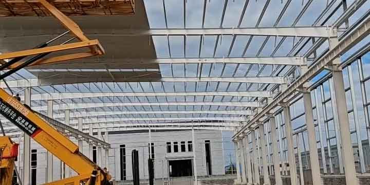 Vista panorámica de una obra de acero blanco con maquinaria elevadora operando en el techo, representativa de un industrial building supplier global.