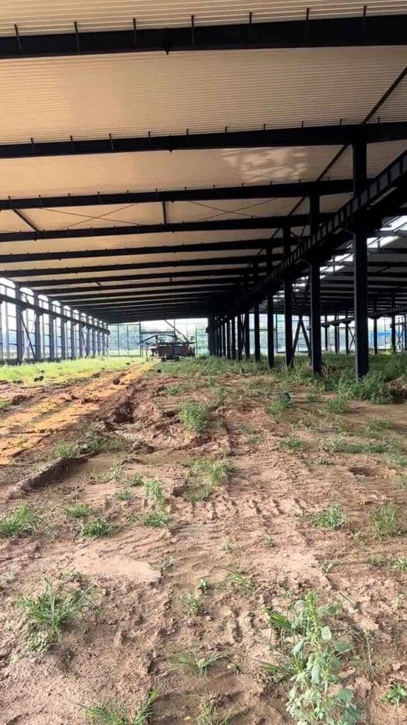 Profundo pasillo interior de una estructura de acero negra mostrando soluciones industriales rápidas con techo instalado sobre suelo fangoso.