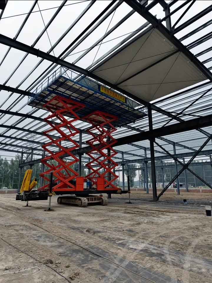 Nave industrial en construcción mostrando el esqueleto de acero desde un ángulo lateral con la plataforma de elevación extendida.