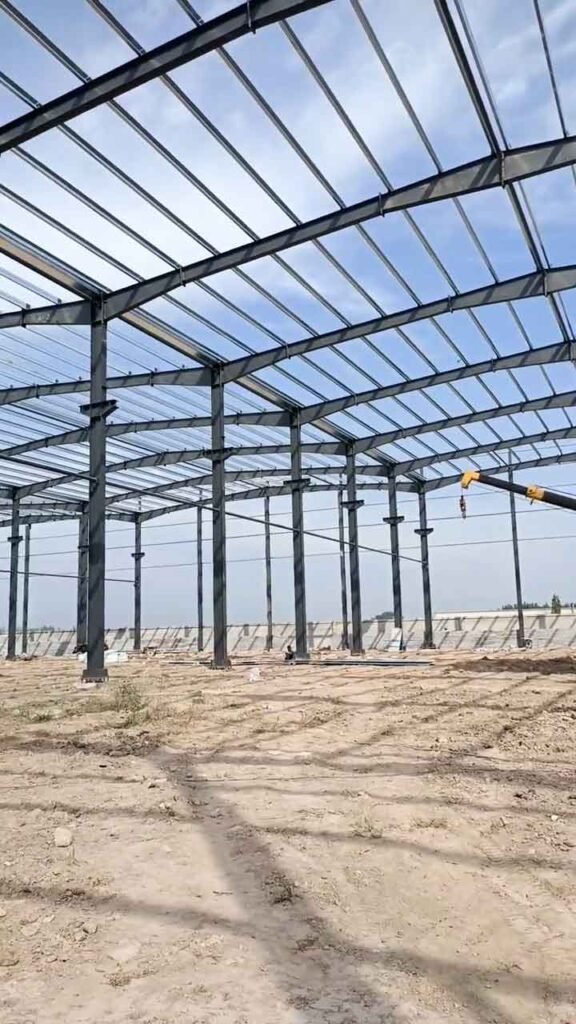 Pilares de acero alineados y cerchas de techo en una obra de galpón metálico con suelo compactado.