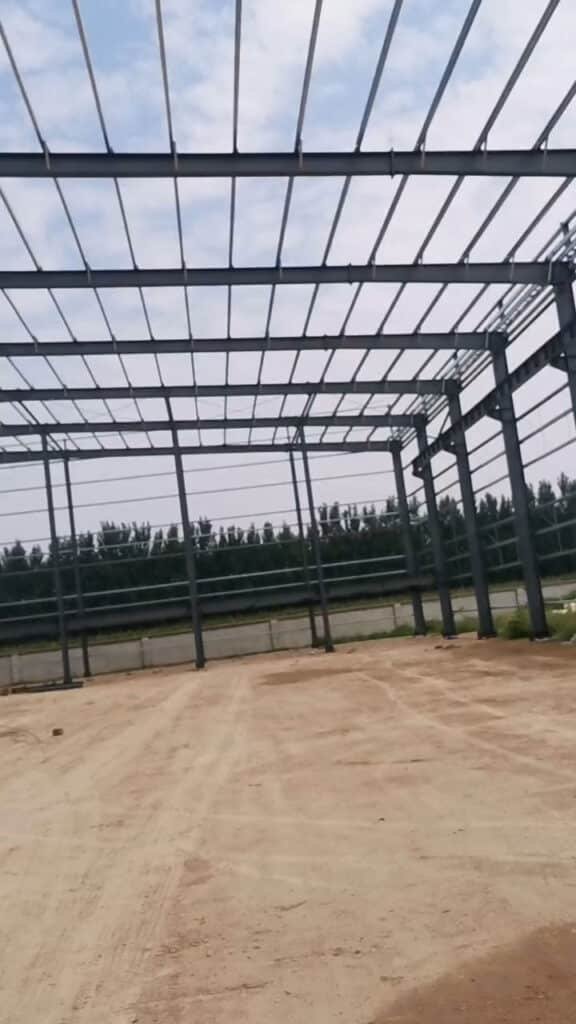 Vista panorámica de un almacén industrial modular en etapa de construcción con maquinaria pesada trabajando en el interior.