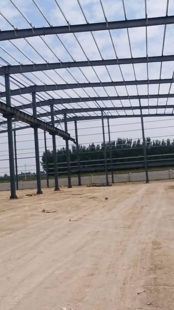 Interior de una bodega con marco de acero mostrando pilares tipo H reforzados y acopio de materiales aislantes en el suelo.