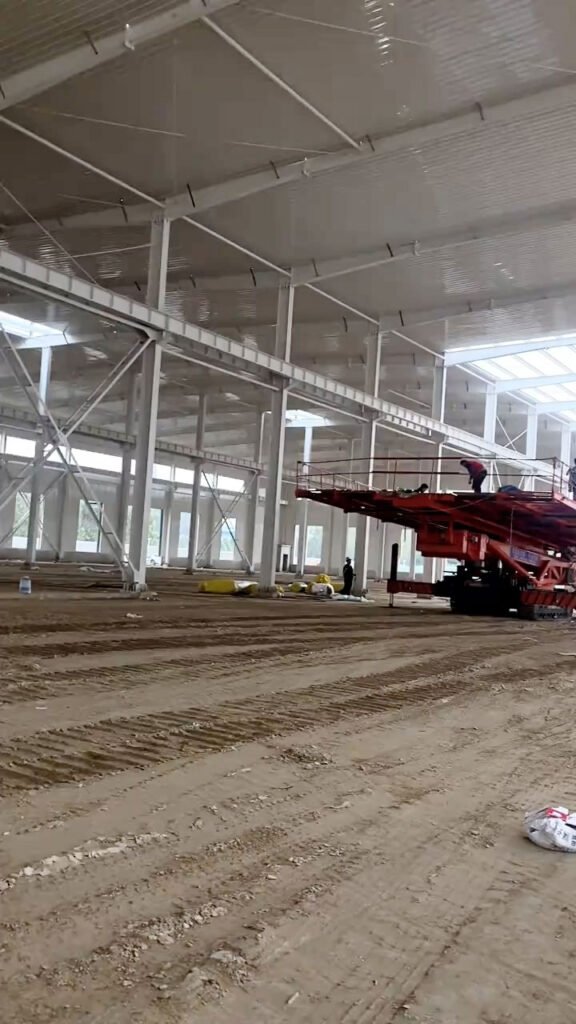 Interior of a clear span warehouse in Australia featuring white structural steel frames and a high-reach lift platform for roof assembly.