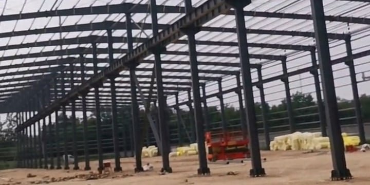 Panorámica de la estructura de un edificio de bodega de acero de gran escala en terreno nivelado y compactado.