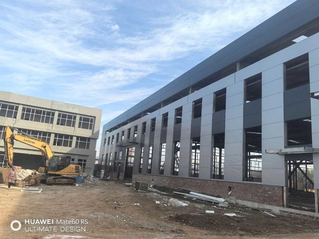 Vista exterior de un edificio industrial con paneles metálicos y maquinaria de excavación LiuGong trabajando en el terreno.