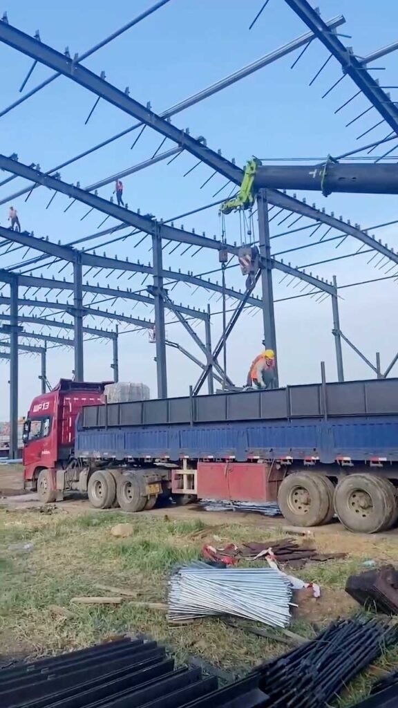 Mobile crane unloading prefabricated steel purlins from a delivery truck on an Australian industrial site.