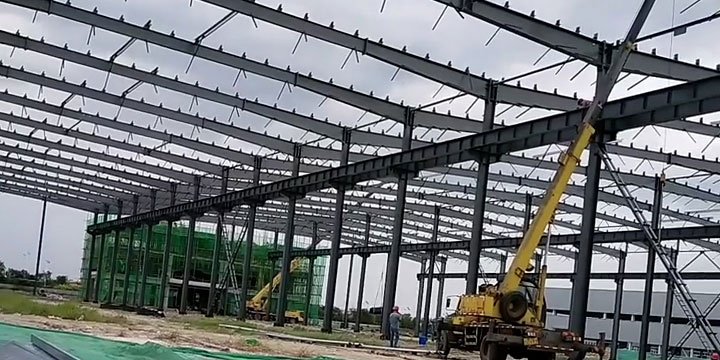 Wide-view perspective of a massive industrial building steel skeleton under construction in a commercial zone
