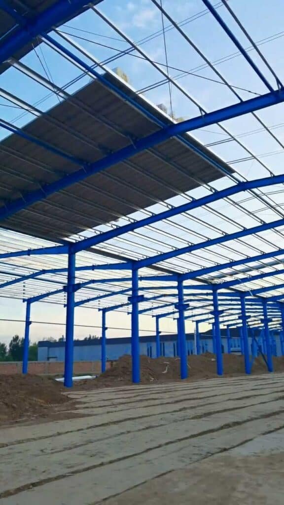 Turnkey construction of a blue steel industrial warehouse by a professional industrial construction company on a prepared dirt foundation.