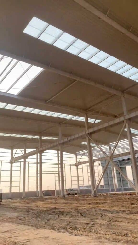 Under-roof view of an industrial steel building highlighting the H-beam connections and roof insulation.