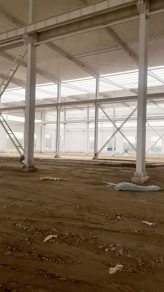 Panoramic perspective of an industrial storage facility frame with white-painted columns and cross-beam structures on a prepared dirt floor.