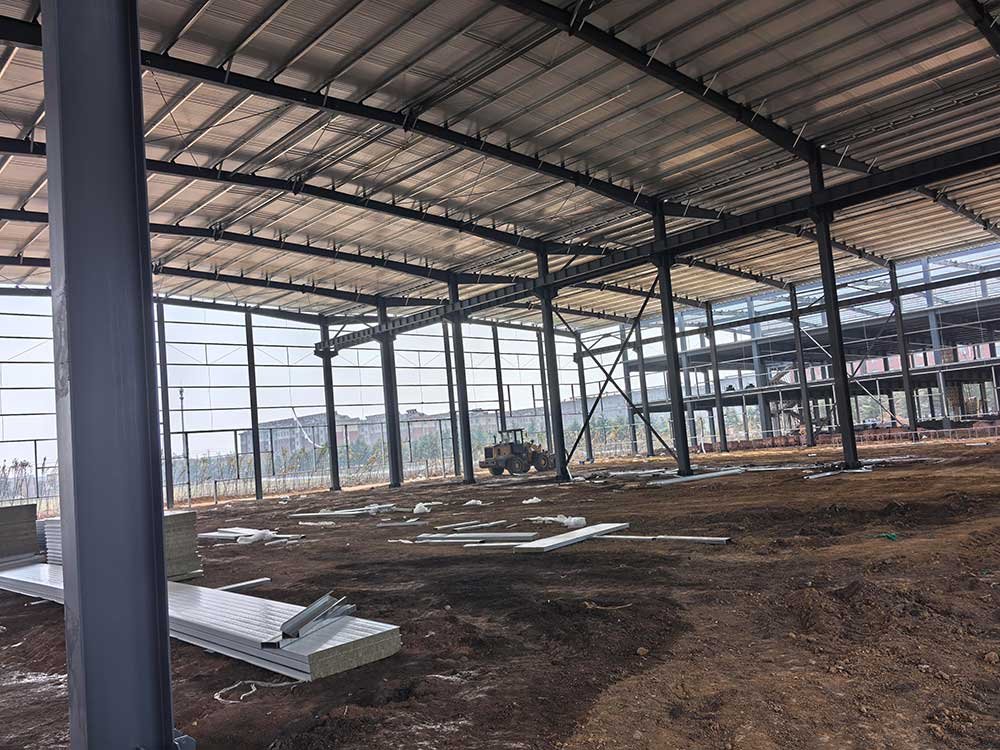 Interior de un edificio de bodega industrial con acopio de paneles de cerramiento y tractor nivelando el terreno.