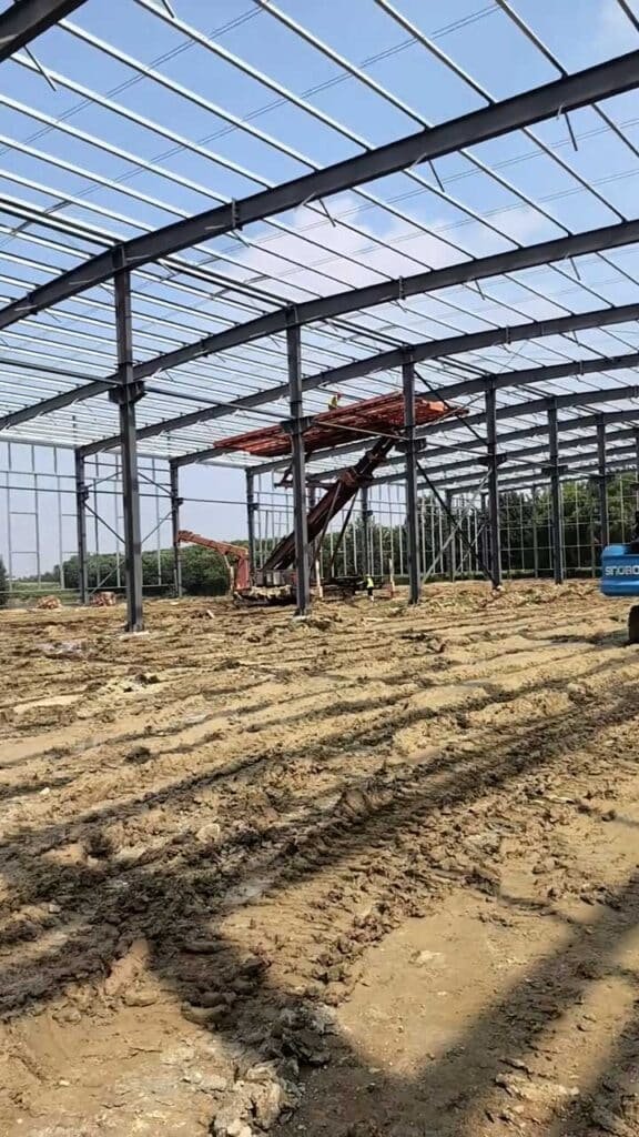 Estructura de un modular steel building en etapa de techado con maquinaria de elevación sobre suelo de arcilla.