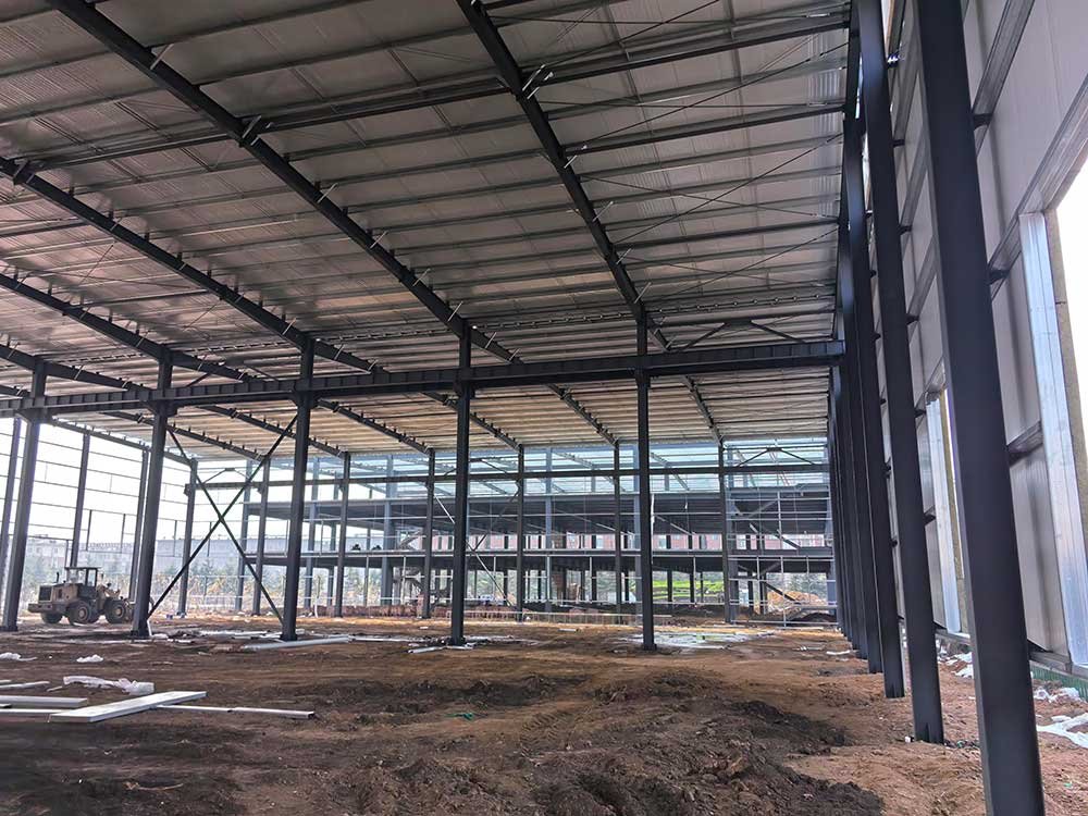 Fase de obra gris de un almacén industrial prefabricado con columnas negras de gran calibre y estructuras secundarias al fondo.
