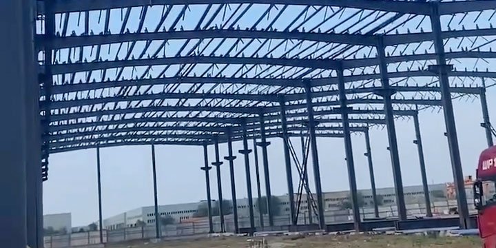 Wide-angle view of a prefabricated industrial steel building profile showing clear-span engineering and local factory backdrop.