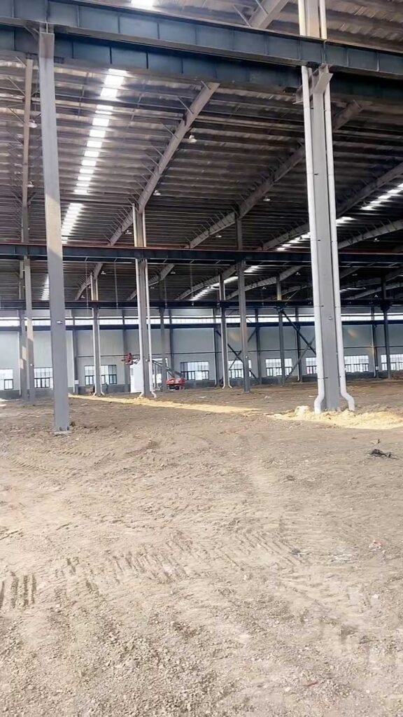 Interior view of a massive prefabricated warehouse under construction in Canada, featuring heavy-duty H-beam columns and natural skylight integration.