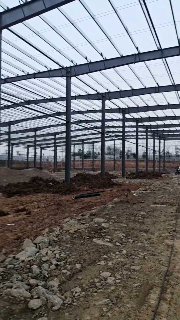 Esqueleto de bodega prefabricada de acero sismorresistente en fase de montaje inicial sobre terreno nivelado.