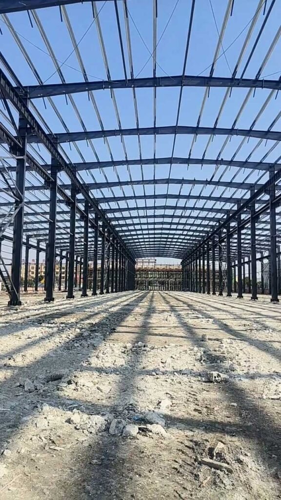 Long interior view of a reinforced warehouse building skeleton, showing rows of structural steel columns on a prepared foundation