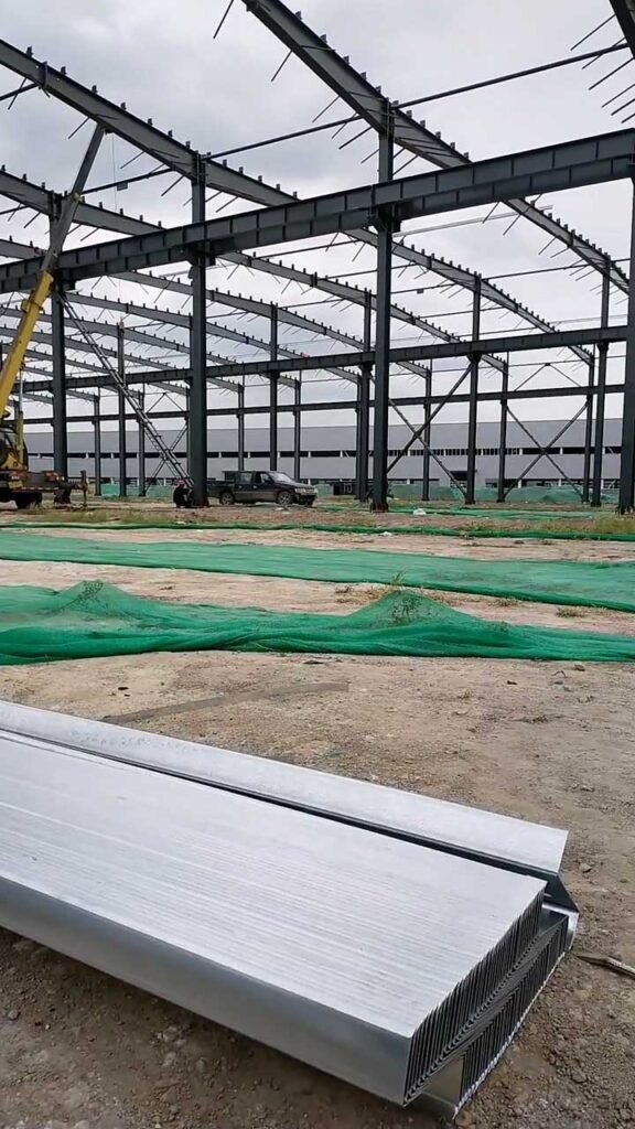 Bundles of galvanized steel purlins and roof panels delivered on-site for a prefabricated industrial project.
