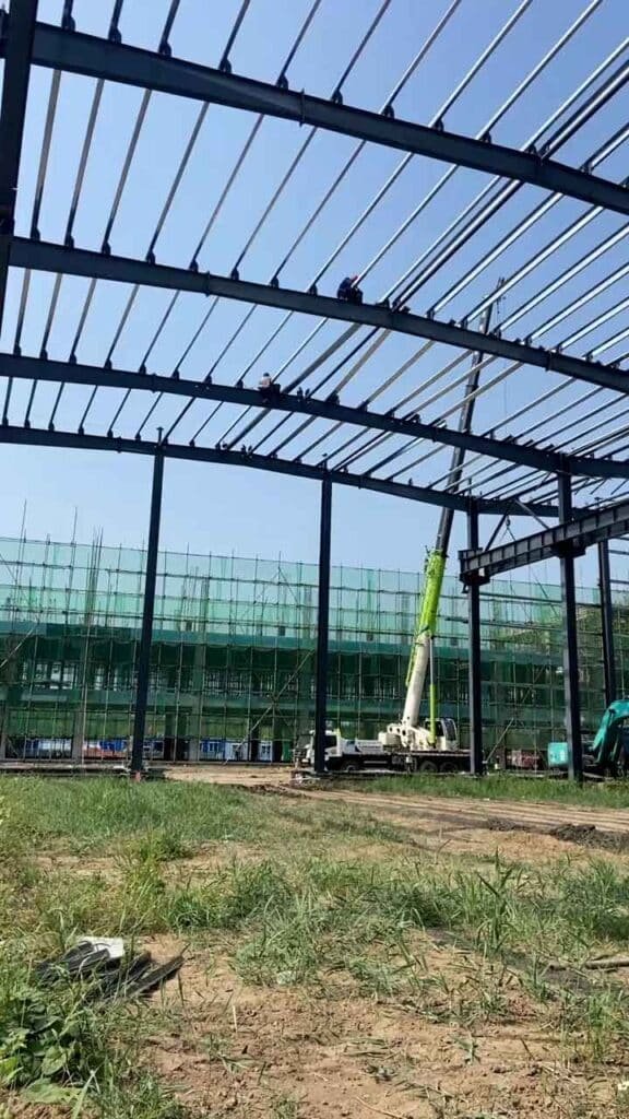Operarios trabajando en el montaje de la techumbre de un steel warehouse building de gran envergadura con grúa de alto alcance.