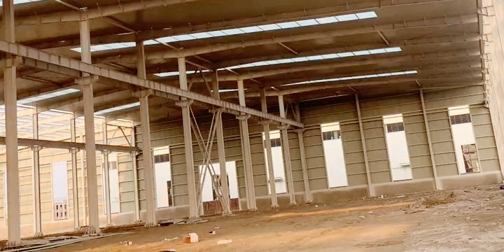 Interior of a large-span industrial shed under construction showing white-painted steel columns and beams.