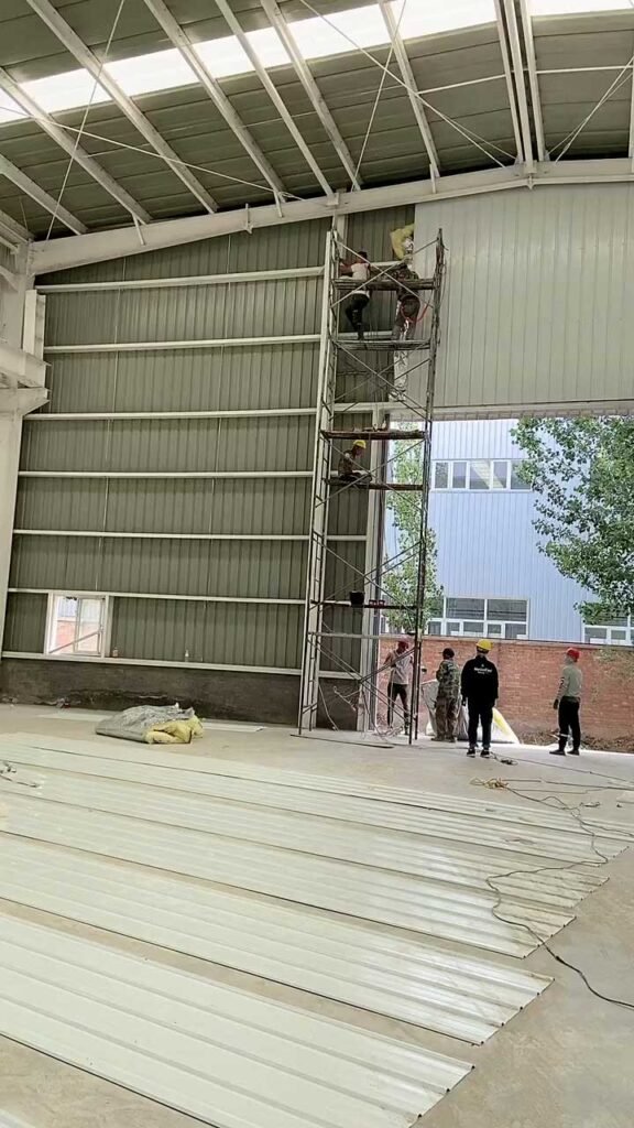 Instalación de paneles de cerramiento en una bodega metálica por operarios especializados en andamios.