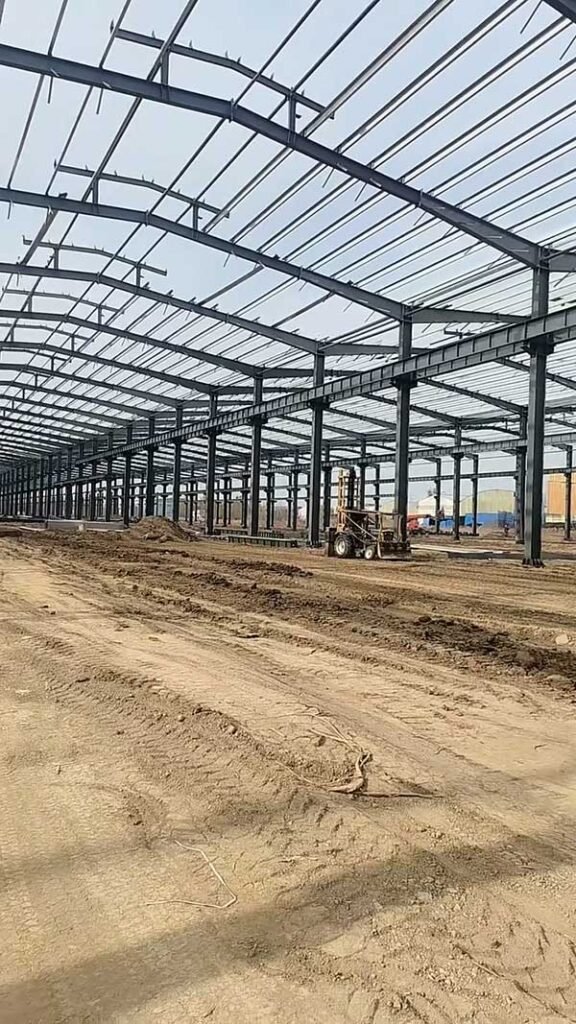 Interior grid of steel roof purlins and rafters installed by an expert warehouse supplier in a dusty environment.