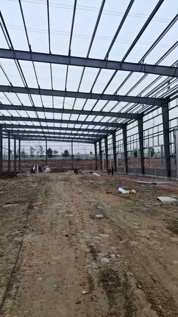 Sistema de bodega de acero con columnas de carga pesada y entramado de techumbre alineado en terreno compactado.
