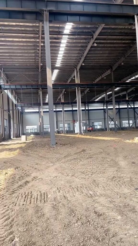 Perspective view of a high-ceiling warehouse building showing the vast floor area and structural steel skeleton ready for floor pouring