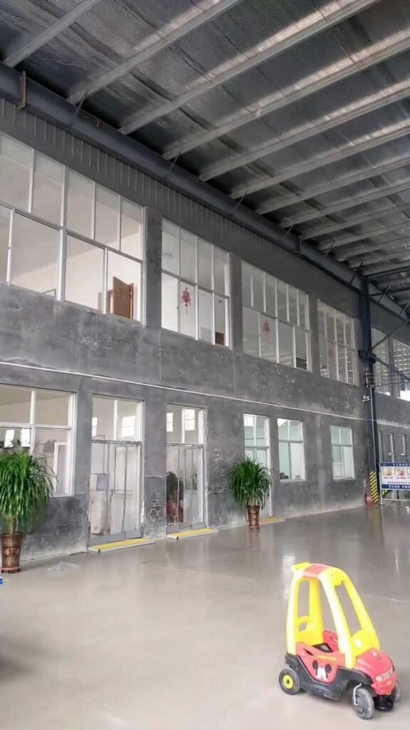 Two-story administrative office built within a steel warehouse frame featuring large windows and concrete finishes.