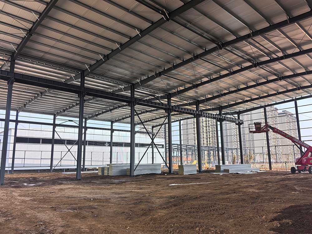 Estructura metálica para almacén en proceso de construcción con plataforma elevadora tipo tijera para el montaje de paneles.